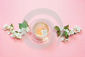 Jasmine flowers and cup of green tea on pink. Top view and concept.