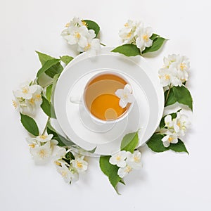 Jasmine leaves and flowers around cup of green tea on white background. Top view and concept.