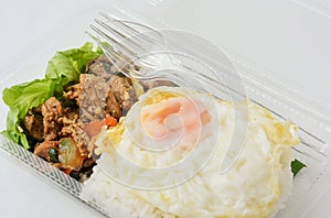 Jasmine rice with spicy pork fried with thai pepper and fried egg in a transparent plastic box package