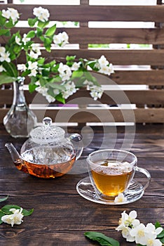 Jasmine tea in transparent cup, jasmine flowers and teapot on wooden table. Copy space. Tea party