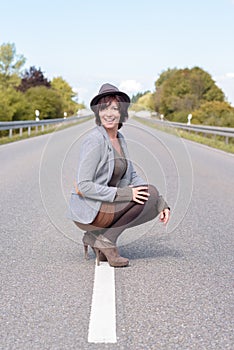 Jaunty trendy young woman crouching on a road