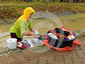 Indonesian woman washes clothes in unsanitary water canal
