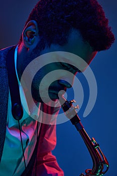 Jazz in modern music. Close up photo of young handsome man playing saxophone in neon light. Gel portraits.