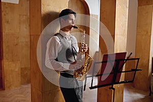 Jazz musician playing saxophone and leaning against art studio wall