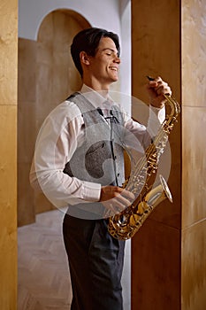 Jazz musician playing saxophone and leaning against art studio wall