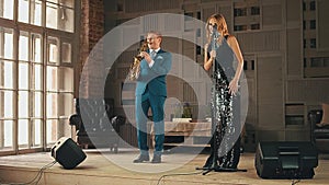 Jazz vocalist in glare dress and saxophonist in blue suit on stage. Performance