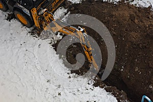 JCB excavator digs a trench for laying a sewer pipe on a cloudy winter day. Selective focus