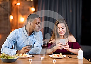 Jealous black guy peeking into girlfriend& x27;s smartphone, reading her messages
