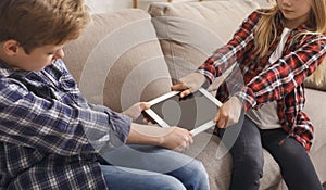 Jealous Brother And Sister Pulling Apart Tablet Sitting On Sofa