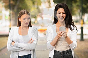 Jealous Girl Looking At Friend`s Phone Walking Together Outdoors