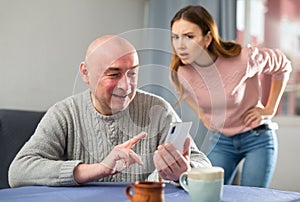 Jealous wife looking at her husband using smartphone