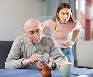 Jealous wife looking at her husband using smartphone