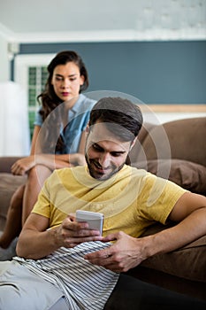 Jealous woman watching man using mobile phone in the living room