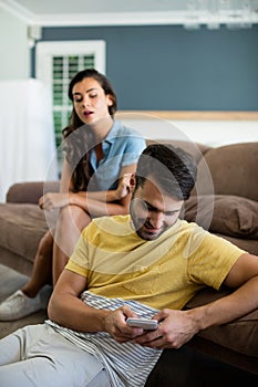 Jealous woman watching man using mobile phone in the living room