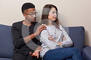 Jealous young European woman doesnt speak to her husband, keeps arms folded, sits back, ingnores communication. Mixed race couple