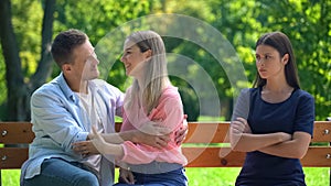 Jealous young woman looking at loving couple sitting park bench, resentment