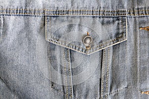 Jean pocket with a metal button in a denim light blue jacket close-up with coarse seams