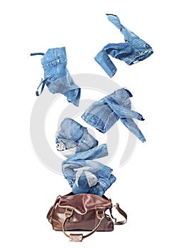 Jeans clothes flying from broun skin luggage bag isolated photo