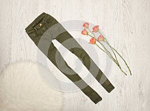 Jeans color khaki, orange roses, white artificial fur on a wooden background. Fashionable concept, top view