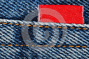 Jeans fabric, seam with orange threads and red sewn label, close-up macro view