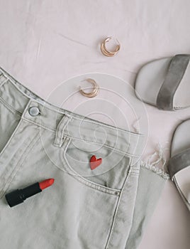 Jeans, sandals and red lipstick on beige background. Overhead view of woman& x27;s casual spring summer outfit. Trendy