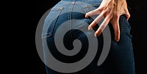Jeans. The young woman holds a hand on buttocks. Luxury manicure and fashion clothes.