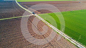 A jeep crossing a country road, off-road aerial view of a car traveling a dirt road through the fields.