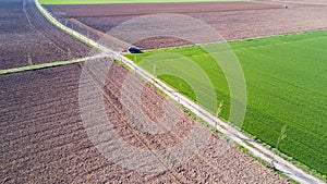 A jeep crossing a country road, off-road aerial view of a car traveling a dirt road through the fields.