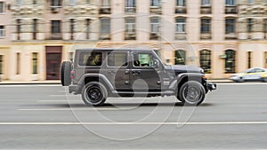 Jeep Wrangler Unlimited Sahara is driving in the cityscape. Side view of gray SUV in motion