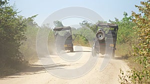 Jeeps drive along brown ground road leaving dust clouds