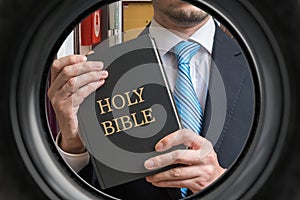 Jehovah witness is showing bible behind door. View from peephole photo