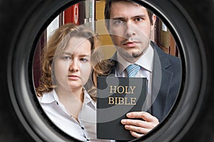 Jehovah witnesses are showing bible behind door. View from peephole