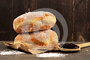 Jelly donuts with spoon of jam against dark wood