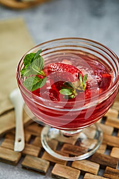 Jelly with strawberries in a glass on a wooden board, against a background of concrete