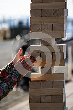 Jenga, girl`s hands try to pull out a wooden block, without tipp