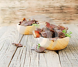 Jerked meat, cow, deer, wild beast or biltong in wooden bowls on a rustic table, selective focus