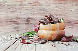 Jerked meat, cow, deer, wild beast or biltong in wooden bowls on a rustic table, selective focus