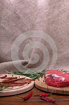 Jerky meat and raw beef on wooden table in front of burlap cloth