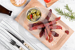 Jerky meat strips with spices, green olives, rosemary on a grey background