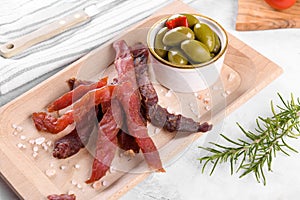 Jerky meat strips with spices, green olives, rosemary on wooden plate