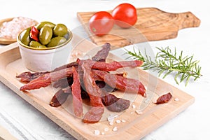 Jerky meat strips with spices, green olives, rosemary on wooden plate
