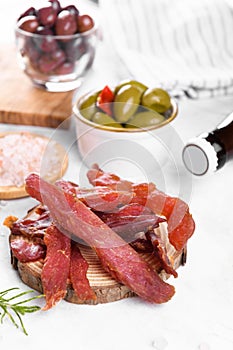 Jerky meat strips with spices, olives, snack for beer on wooden plate