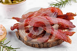 Jerky meat strips with spices, olives, snack for beer on wooden plate, close up