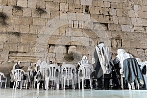 JERUSALEM ISRAEL - Octobe 24, 2018: Men in white tallits sitting on white chairs and praying to their religion at the Wailing Wall