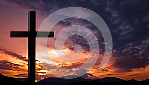 Jesus Christ cross, wooden crucifix on a heavenly background with dramatic light and clouds and colorful orange sunset