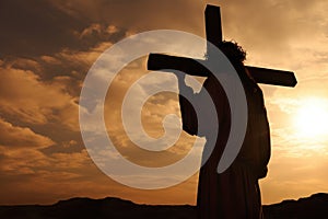 Jesus Christ holding the cross at sunset