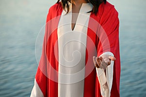 Jesus Christ reaching out his hand near water outdoors, closeup