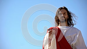 Jesus reaching out hand against blue sky, forgiveness and salvation of sinners