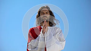 Jesus in robe praying against blue sky background, asking God to forgive sinners