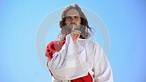 Jesus showing silence gesture on sky background, speechless prayer, deep faith